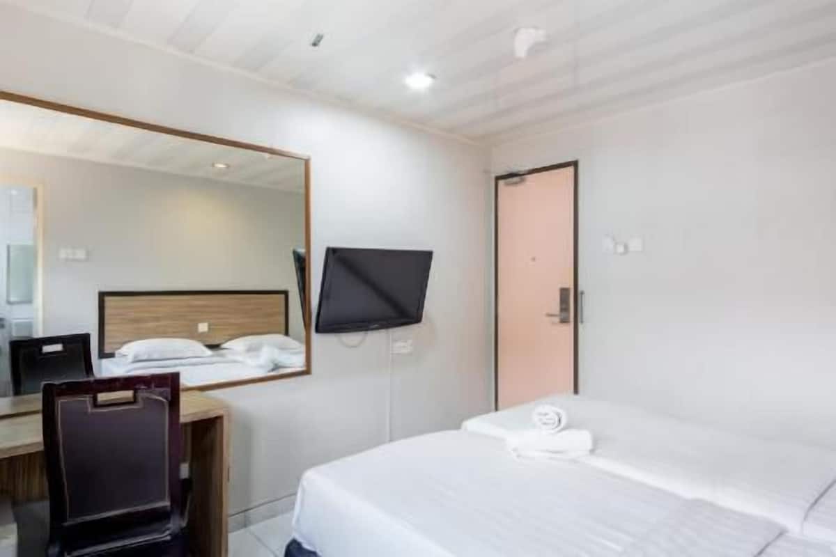 A hotel room with a bed, a desk with a chair, a television mounted on the wall, and a door.