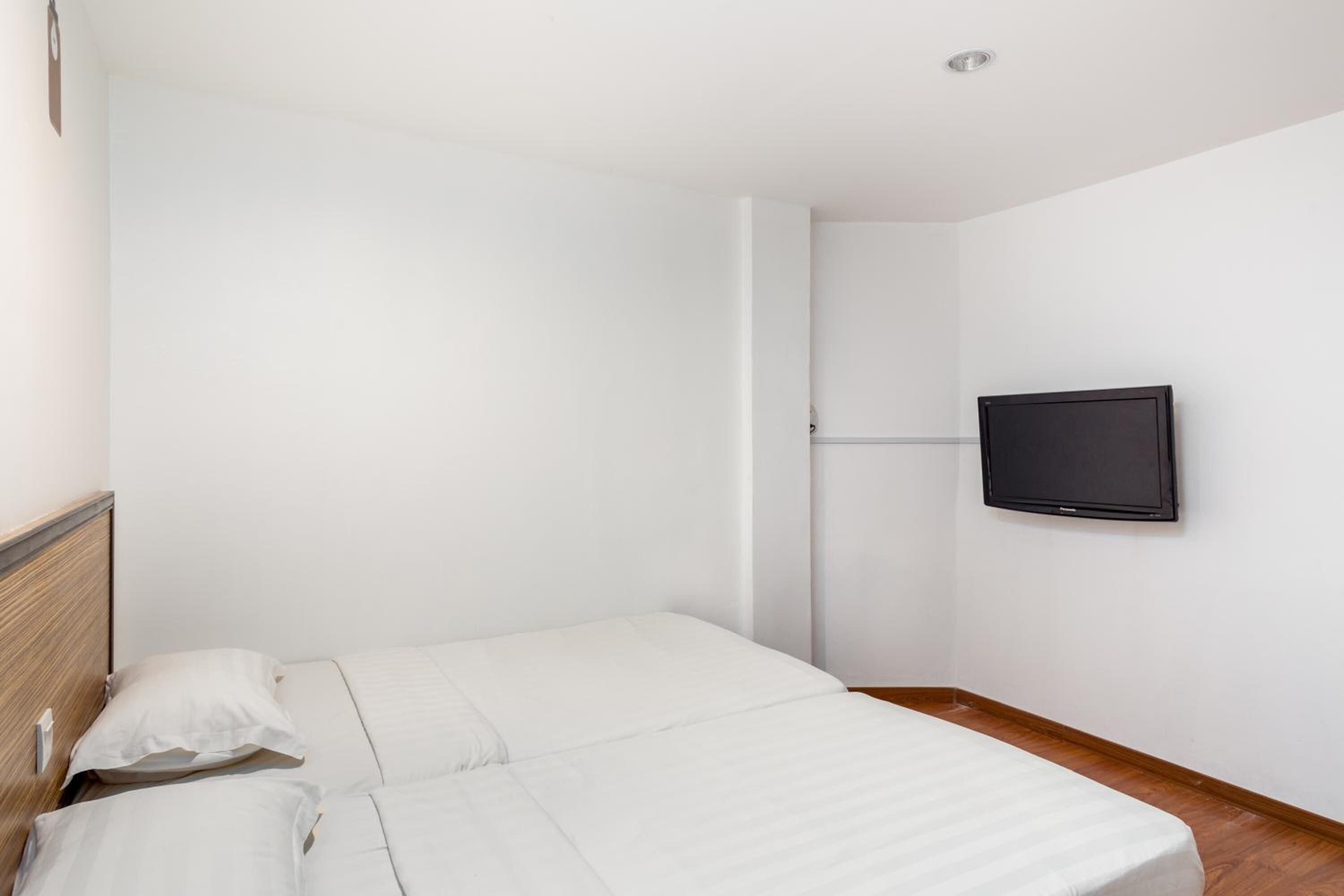 A bedroom with two beds, a television mounted on the wall, and a wooden floor.