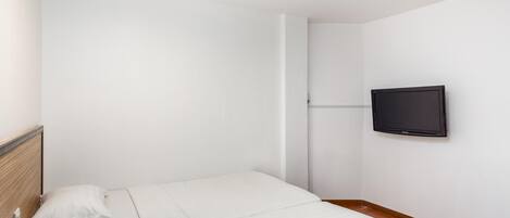 Een slaapkamer met twee bedden, een aan de muur bevestigde televisie en een houten vloer.