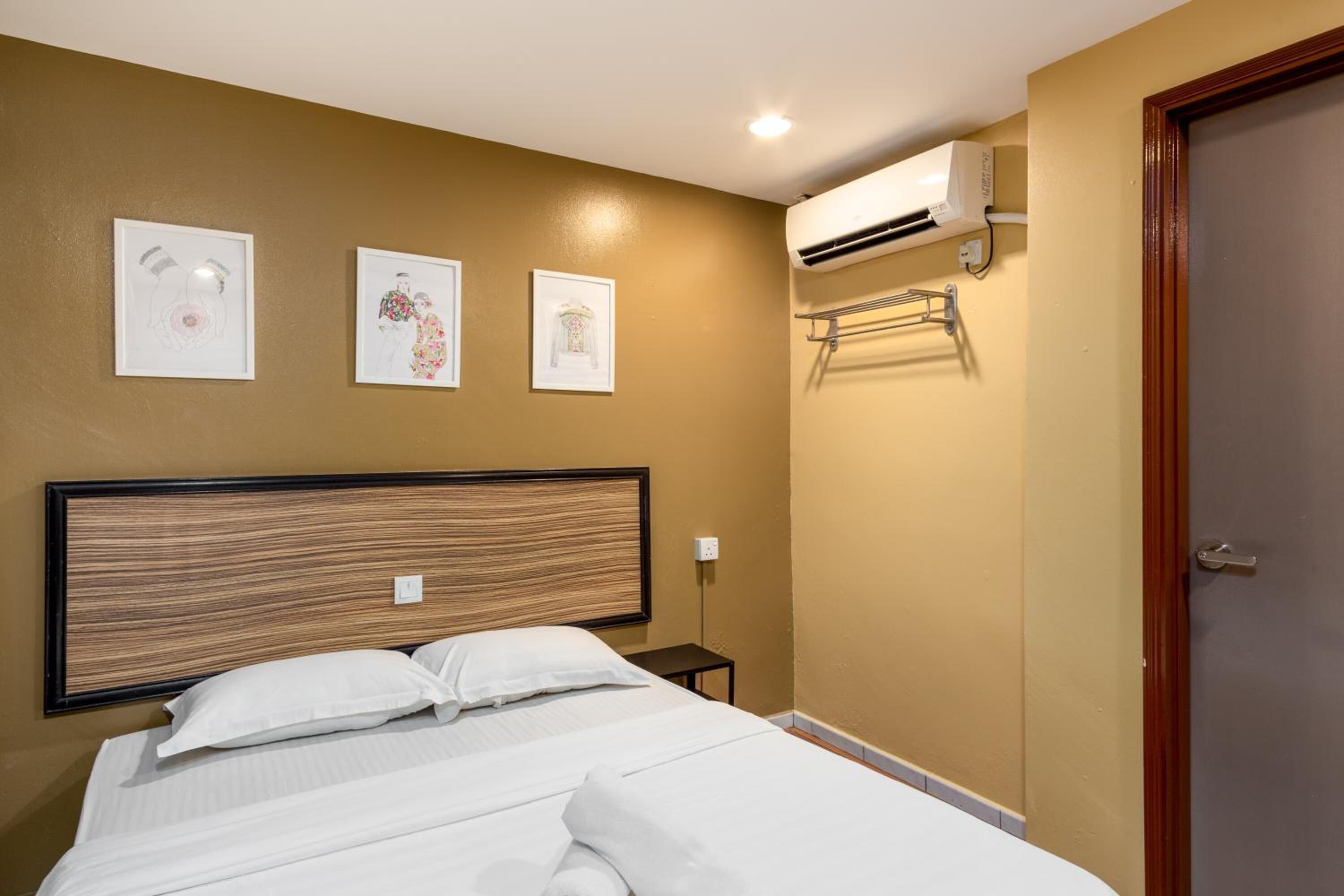 A hotel room with a bed, wall-mounted air conditioning unit, and three framed pictures on the wall.