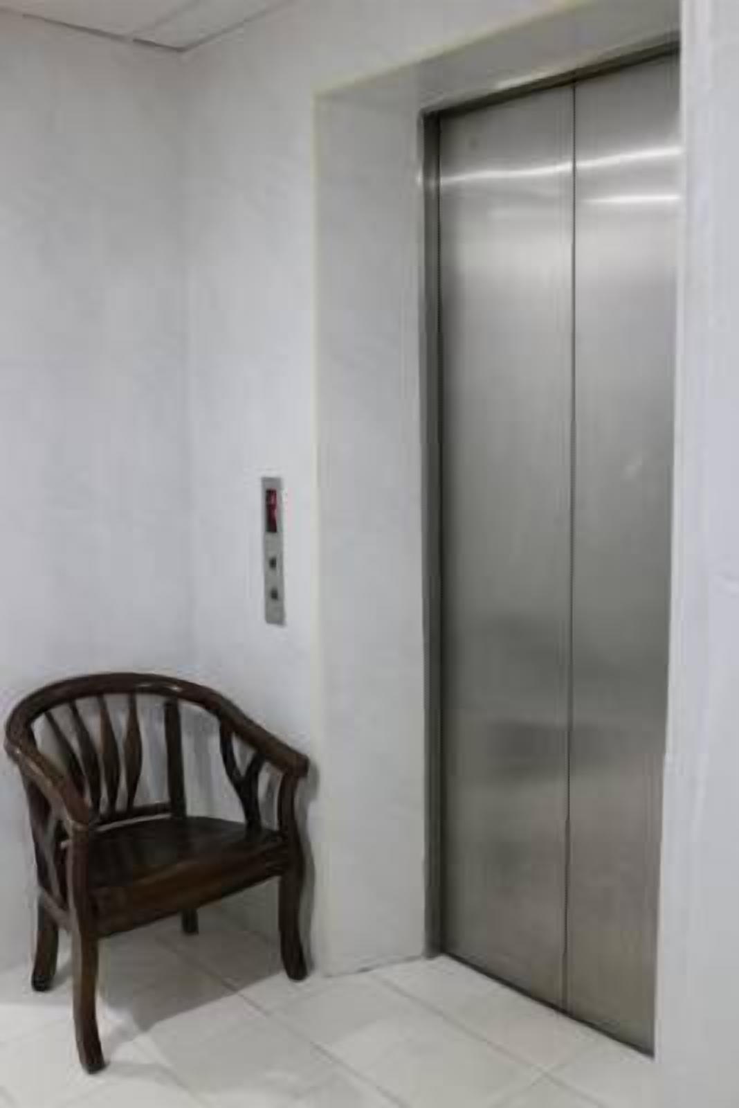 A corner of a room with a wooden chair and a metallic elevator.