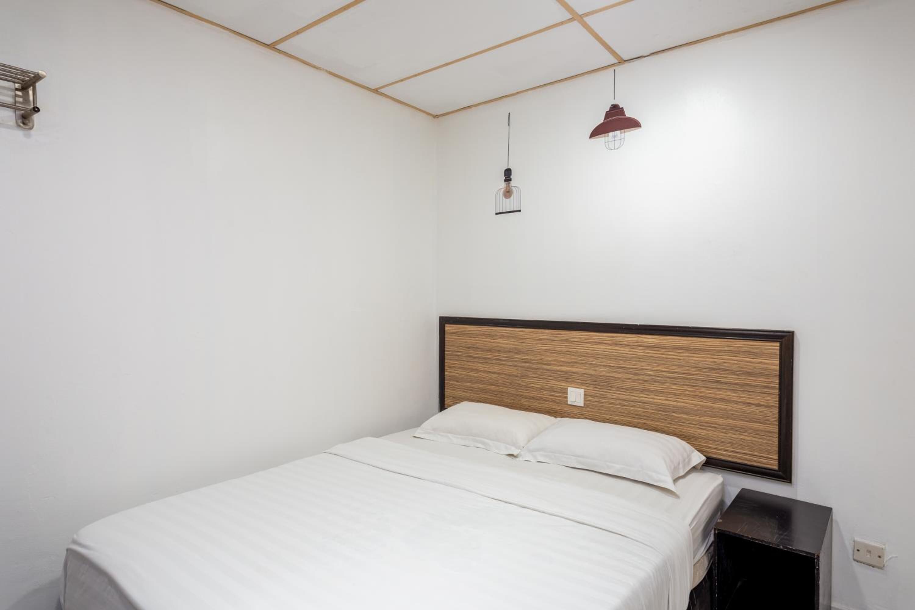 A single bed with a wooden headboard, a bedside table, and a hanging pendant light.