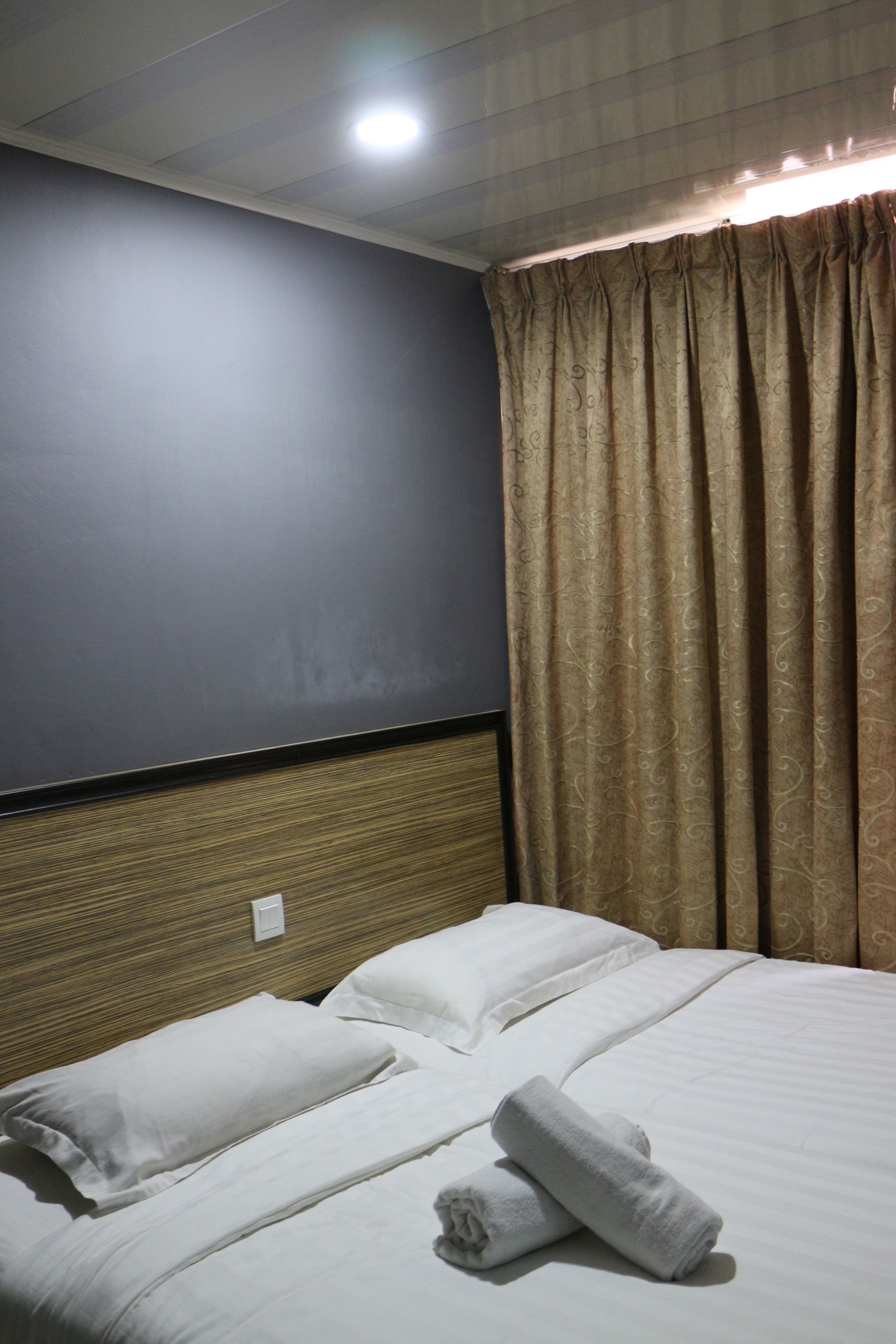 A hotel room with a bed, white linens, a headboard, and a window with curtains.