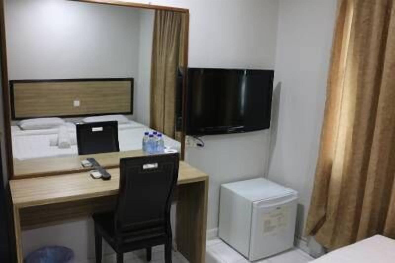 Une chambre d’hôtel compacte comprenant un lit, un bureau avec une chaise, un téléviseur fixé au mur et un petit réfrigérateur.
