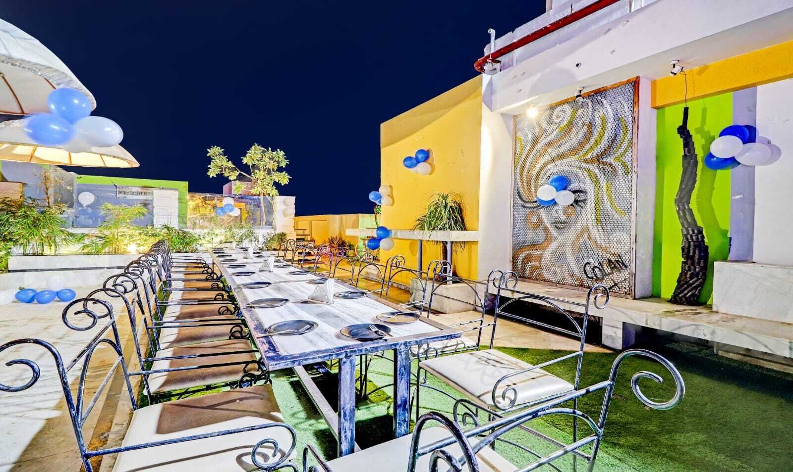 Un área de comedor al aire libre con sillas y mesas de metal, decorada con globos y plantas.