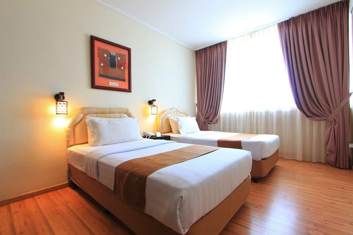 Habitación de hotel con dos camas, suelo de madera y una ventana con cortinas.