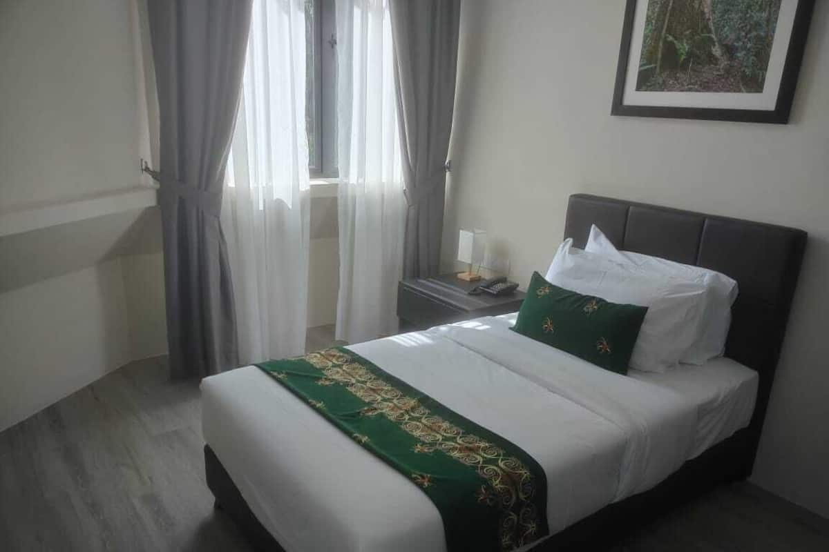 Una cama bien hecha con una colcha verde y blanca, una mesita de noche con una lámpara y un cuadro enmarcado en la pared.