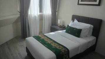 A neatly made bed with a green and white bedspread, a nightstand with a lamp, and a framed picture on the wall.