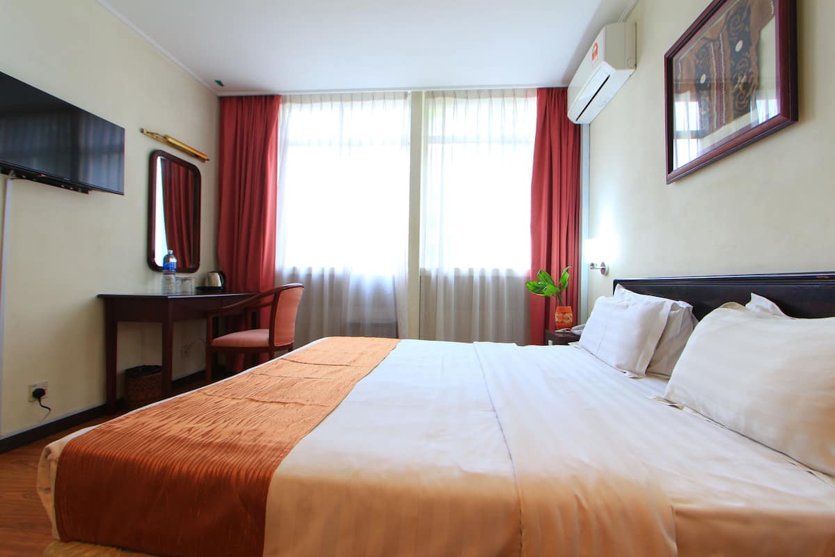 Habitación de hotel con cama, escritorio, silla, televisión y ventana con cortinas.