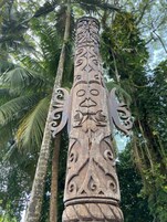 Un poste de madera tallada con diseños intrincados, rodeado de frondosa vegetación.