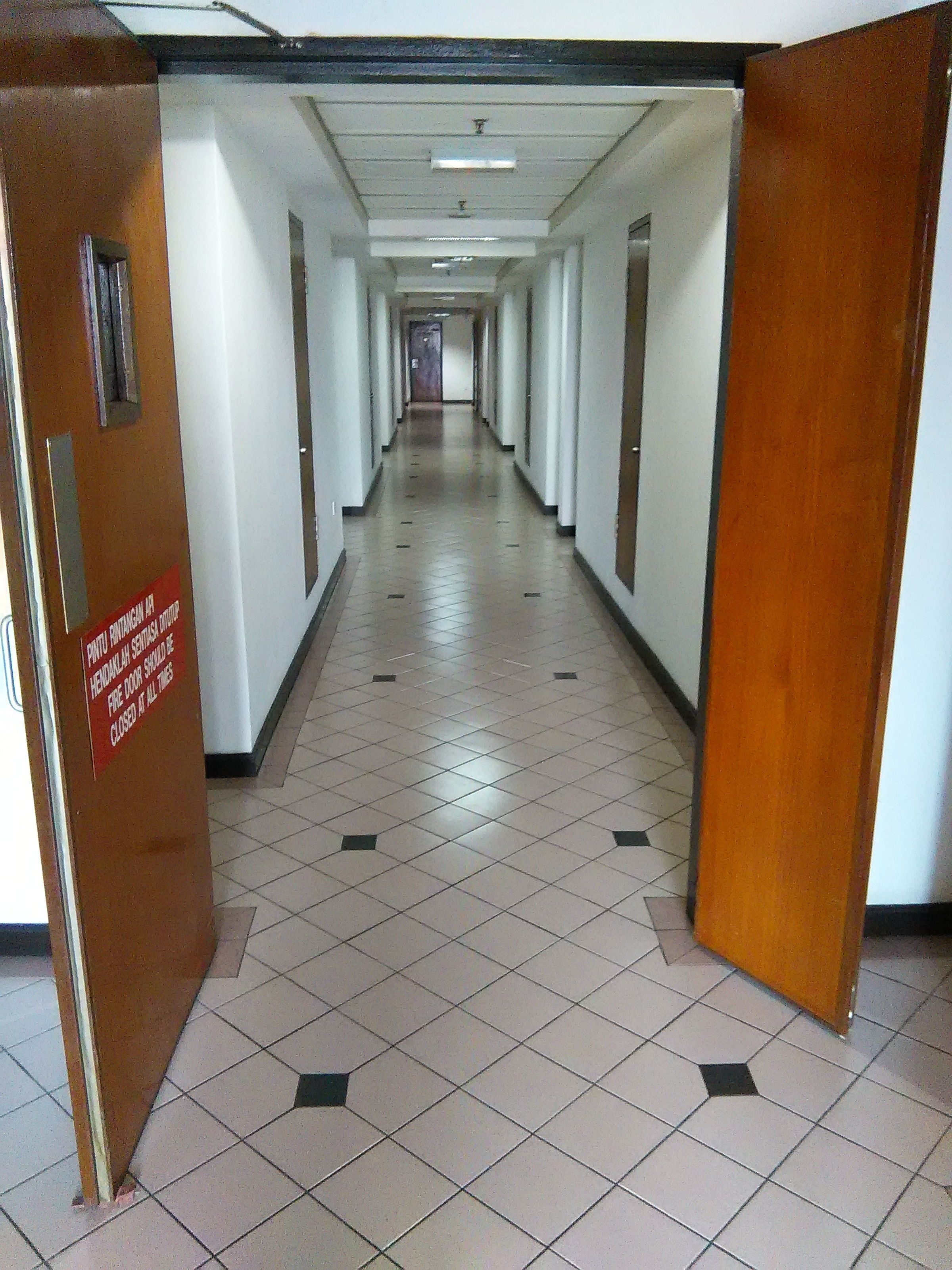 A long, narrow hallway with tiled floors and wooden doors on either side.