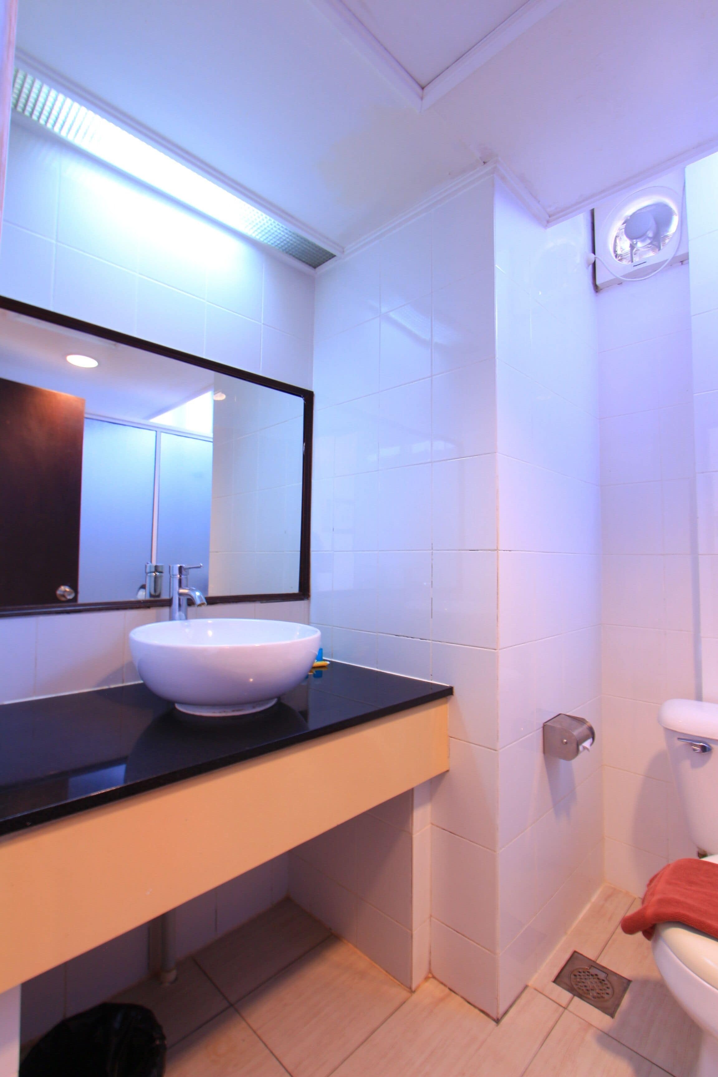 Une salle de bain moderne avec un lavabo blanc, un plan de toilette noir et un grand miroir.