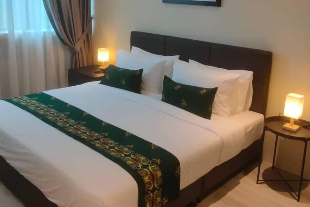 Una habitación de hotel con una cama grande, una mesita de noche con lámpara, un equipo de aire acondicionado y un cuadro en la pared.
