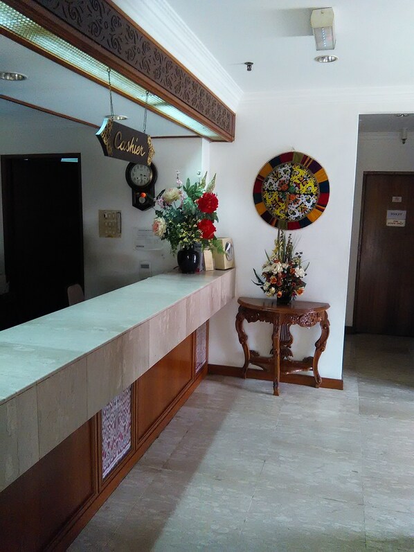 A reception area with a counter, a clock, a wall-mounted decorative plate, and a small table with flowers. - Telang Usan Hotel (Kuching)