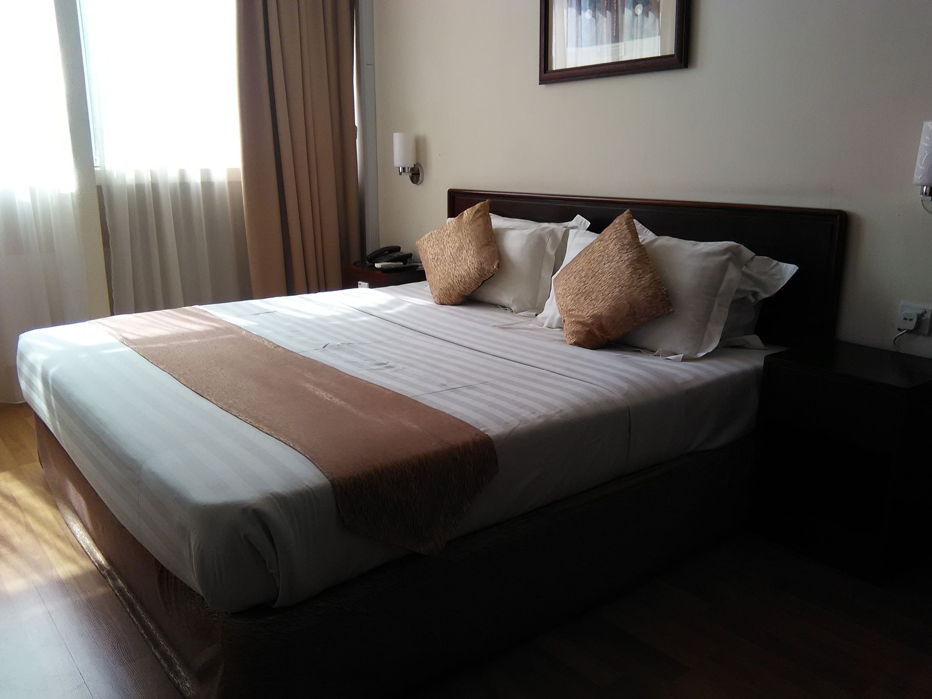 A neatly made bed with a striped bedspread, two pillows, and a brown throw blanket.