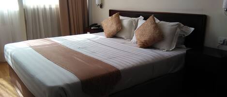 A neatly made bed with a striped bedspread, two pillows, and a brown throw blanket.