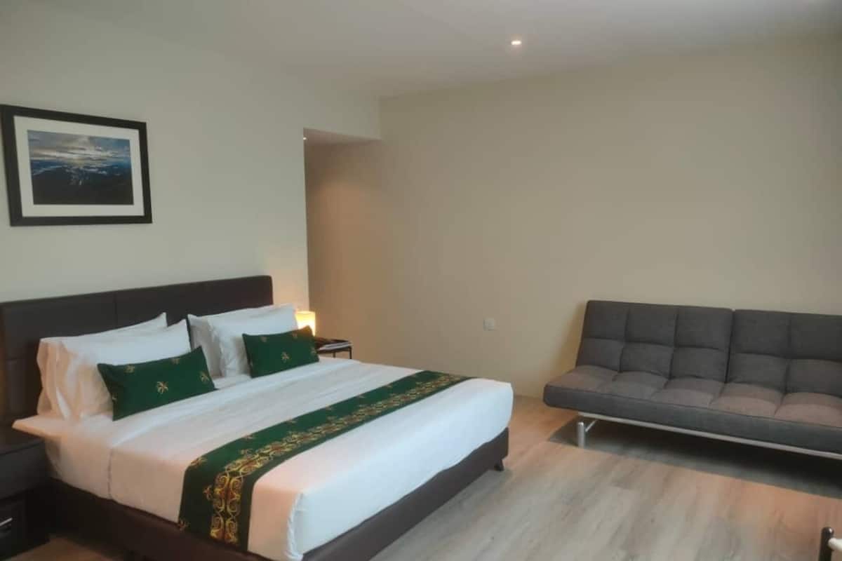 Una cama bien tendida con ropa de cama verde y blanca, un sofá gris y un cuadro en la pared.