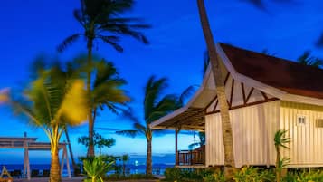 A beachfront building with a covered porch, palm trees, and a view of the ocean.