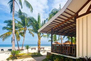 A beachside resort with a covered patio, palm trees, and a view of the ocean.