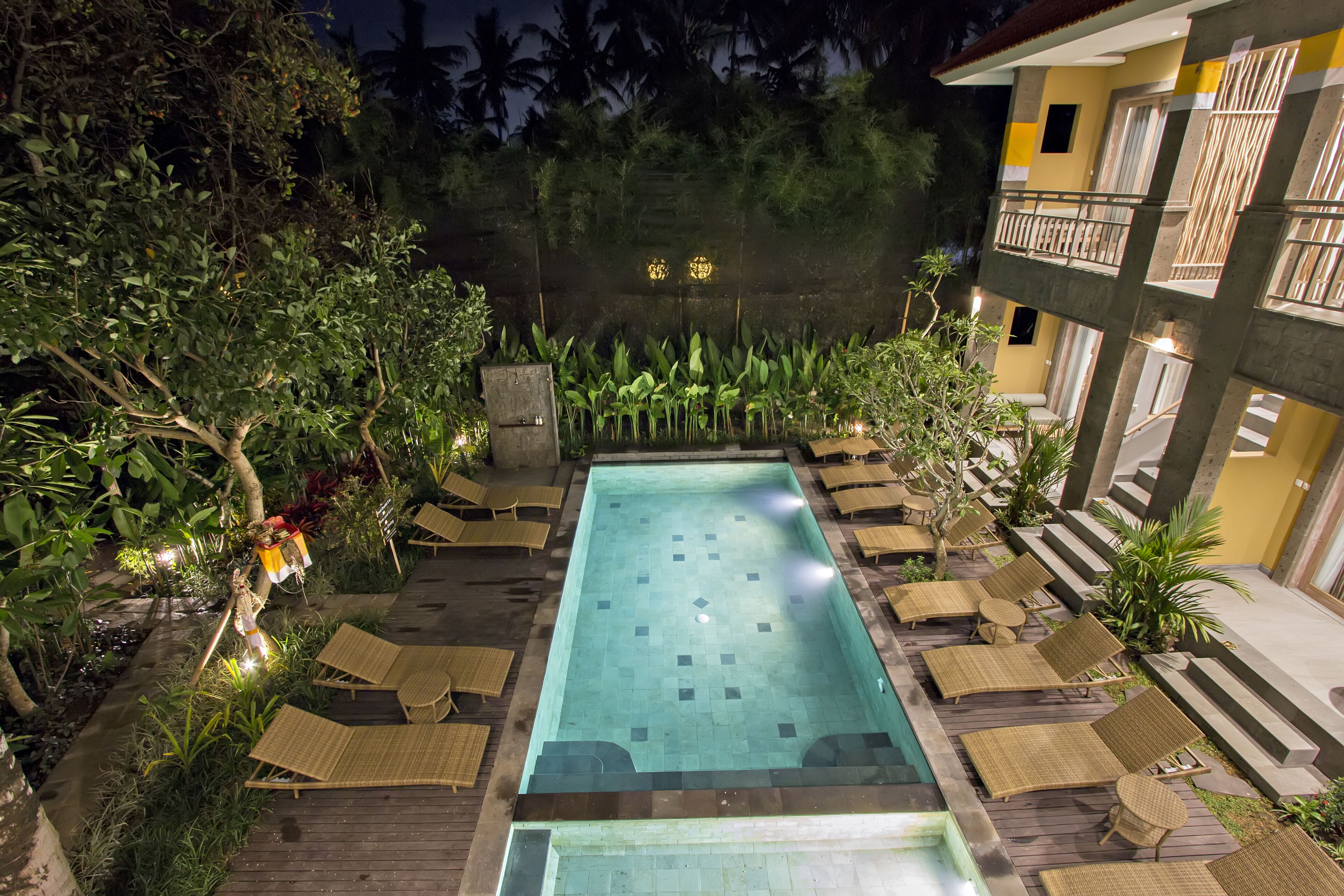 Une piscine rectangulaire entourée d’une terrasse en bois, aménagée avec des chaises longues et des tables.