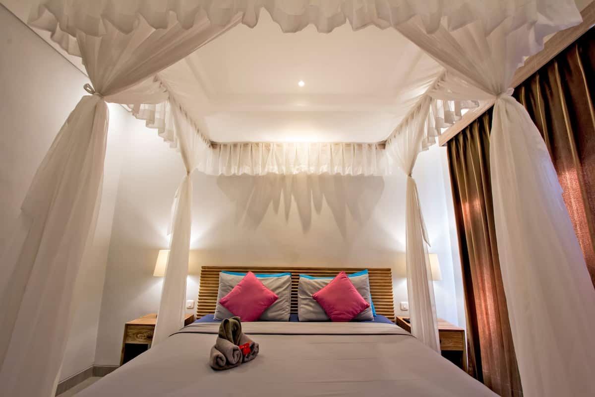 A bedroom with a canopy bed, two pillows, a bedside table, and a lamp.
