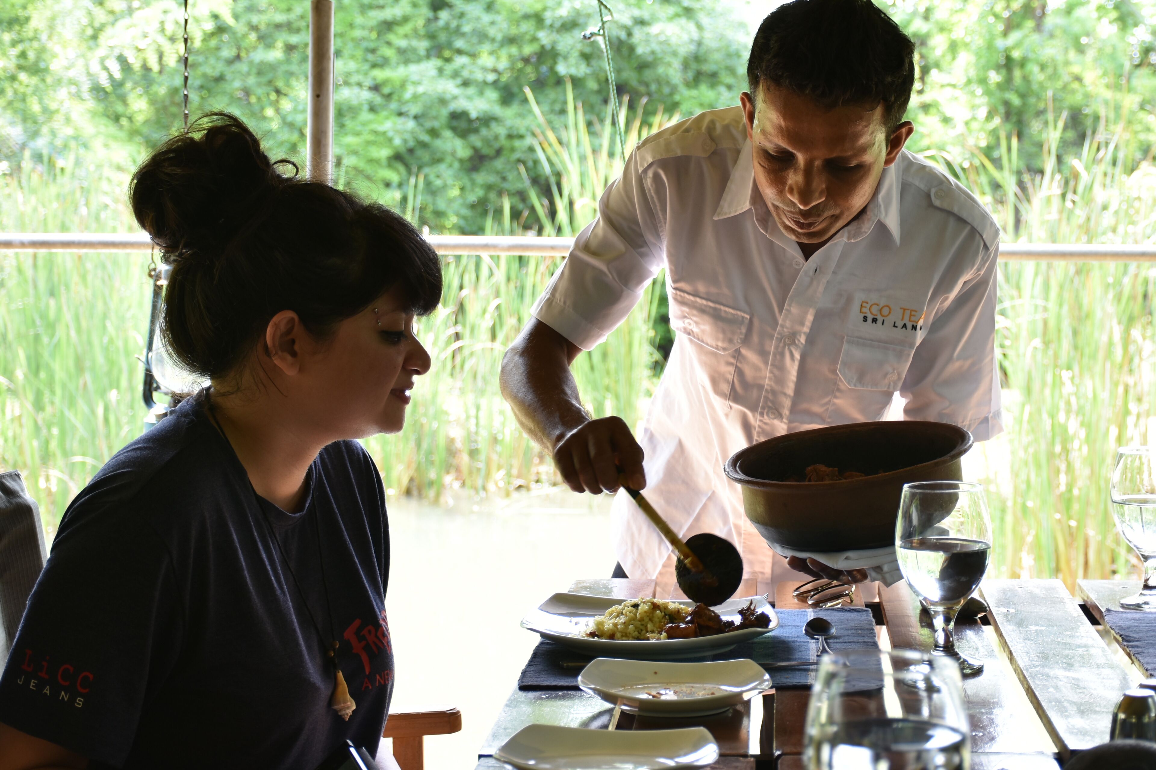 Una persona sirve comida de una olla grande a un plato sobre una mesa de madera.
