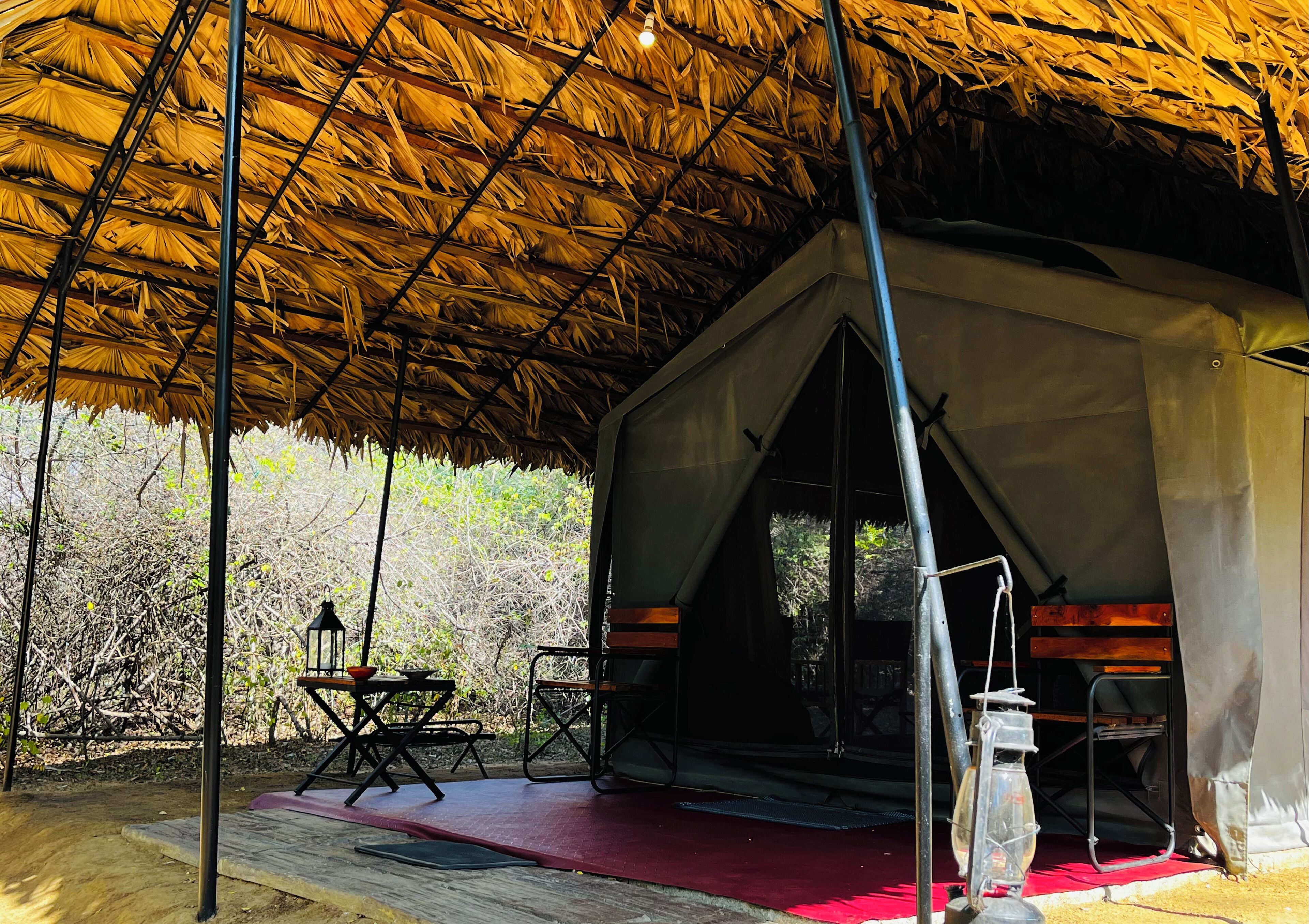 A tent with a thatched roof, a picnic table, and a lantern.