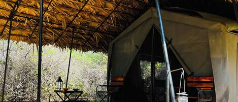 A tent with a thatched roof, a picnic table, and a lantern.
