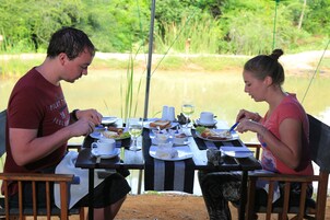 Dos personas cenando en una mesa al aire libre con vista a un lago y vegetación.