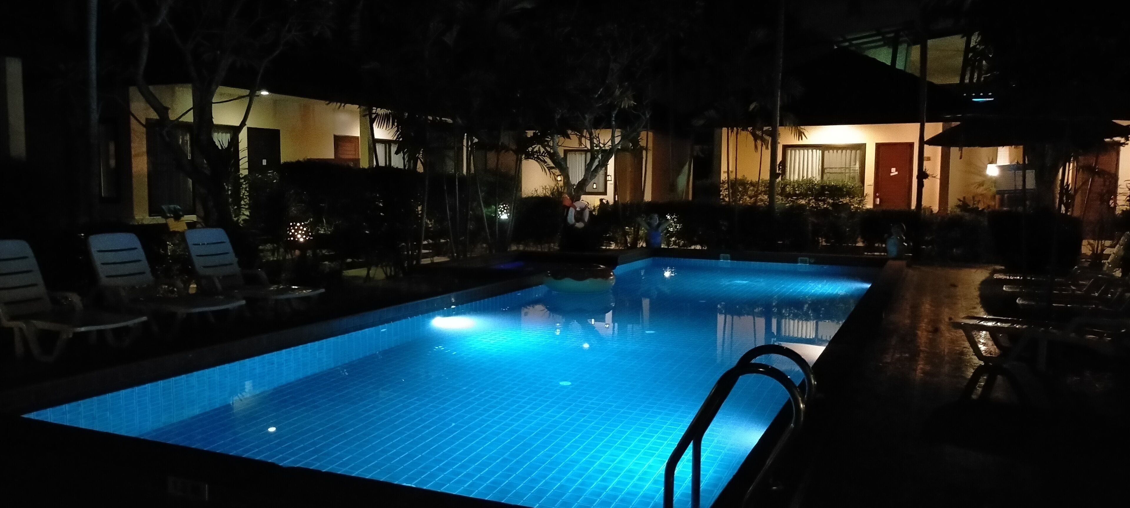 A nighttime swimming pool with lounge chairs and a building in the background.