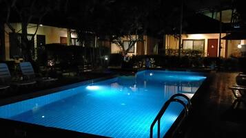 A nighttime swimming pool with lounge chairs and a building in the background.