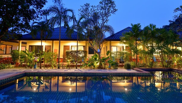 A hotel with a swimming pool, palm trees, and a well-lit exterior at dusk. - Happy Cottages Phuket (Chalong)