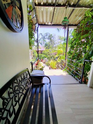 A covered outdoor area with a bench, metal railing, and greenery. - Happy Cottages Phuket (Chalong)