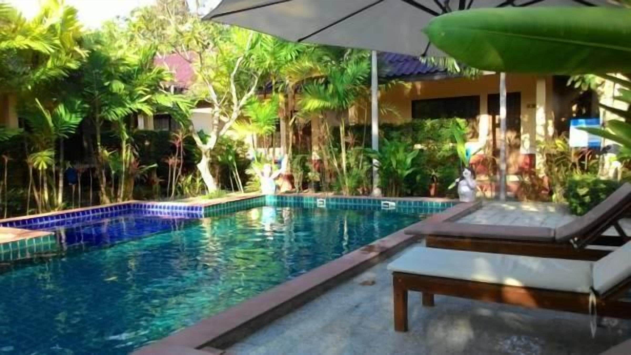 A swimming pool with lounge chairs and umbrellas, surrounded by tropical vegetation.