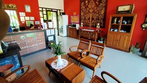 A reception area with wooden furniture, a reception desk, a large tapestry, and a cabinet with decorative items. - Happy Cottages Phuket (Chalong)