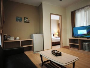 A hotel room with a bed, a television, a small refrigerator, a coffee machine, and a table with a tray. - Happy Cottages Phuket (Chalong)