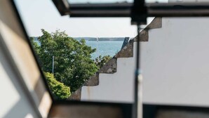 Blick durch ein Fenster auf ein Gewässer, Bäume und ein Gebäude.
