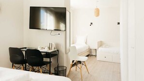 Ein modernes Hotelzimmer mit einem flachbildfernseher an der Wand, einem Schreibtisch mit zwei Stühlen, einer weißen Couch und einem kleinen Beistelltisch.