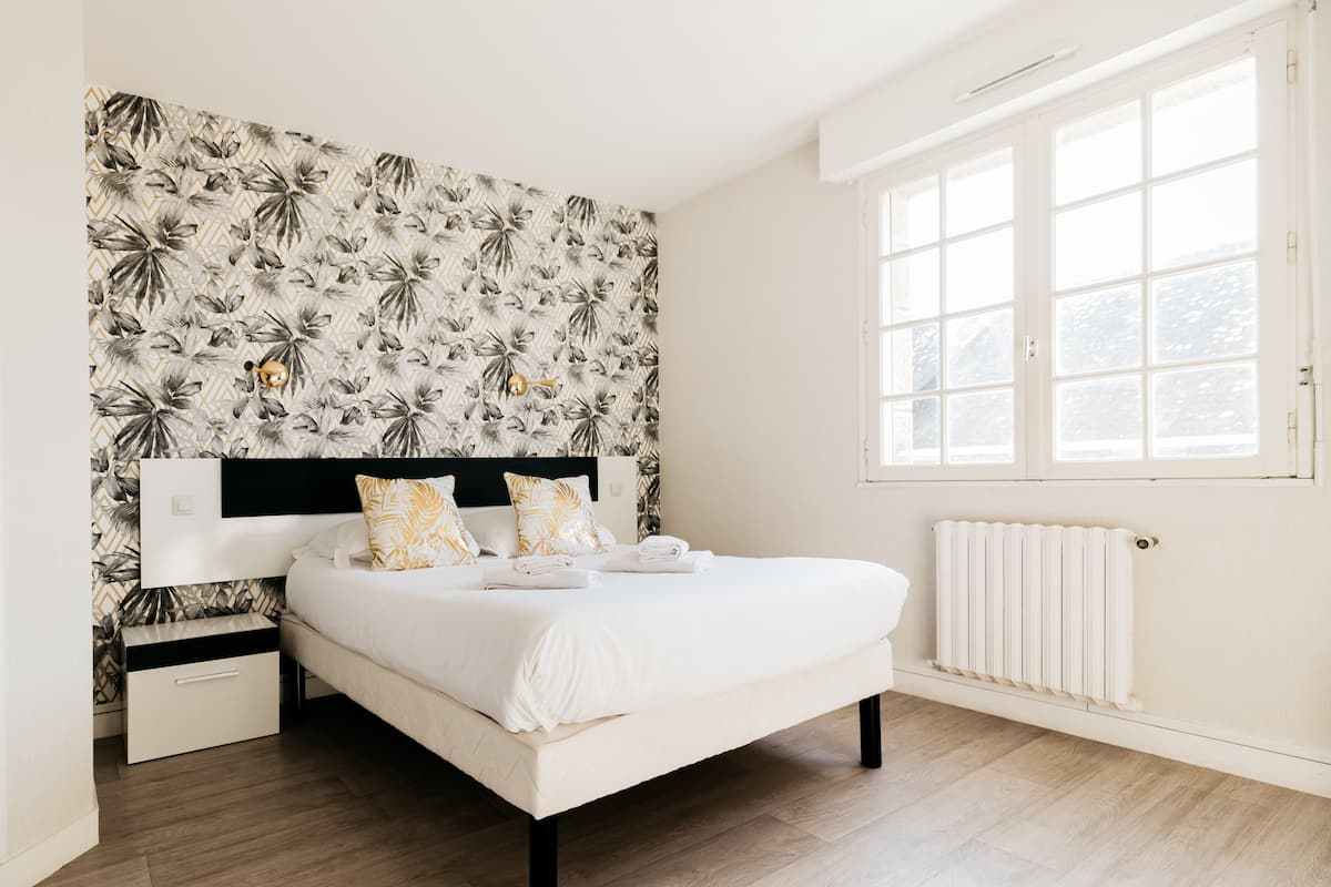 Une chambre à coucher comprenant un lit, une table de chevet, un radiateur et une fenêtre donnant sur des arbres.