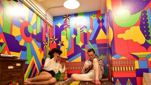A vibrant room with colorful geometric patterns on the walls, a small wooden table, and a patterned cushion. - Vimarn Hostel (Bangkok)