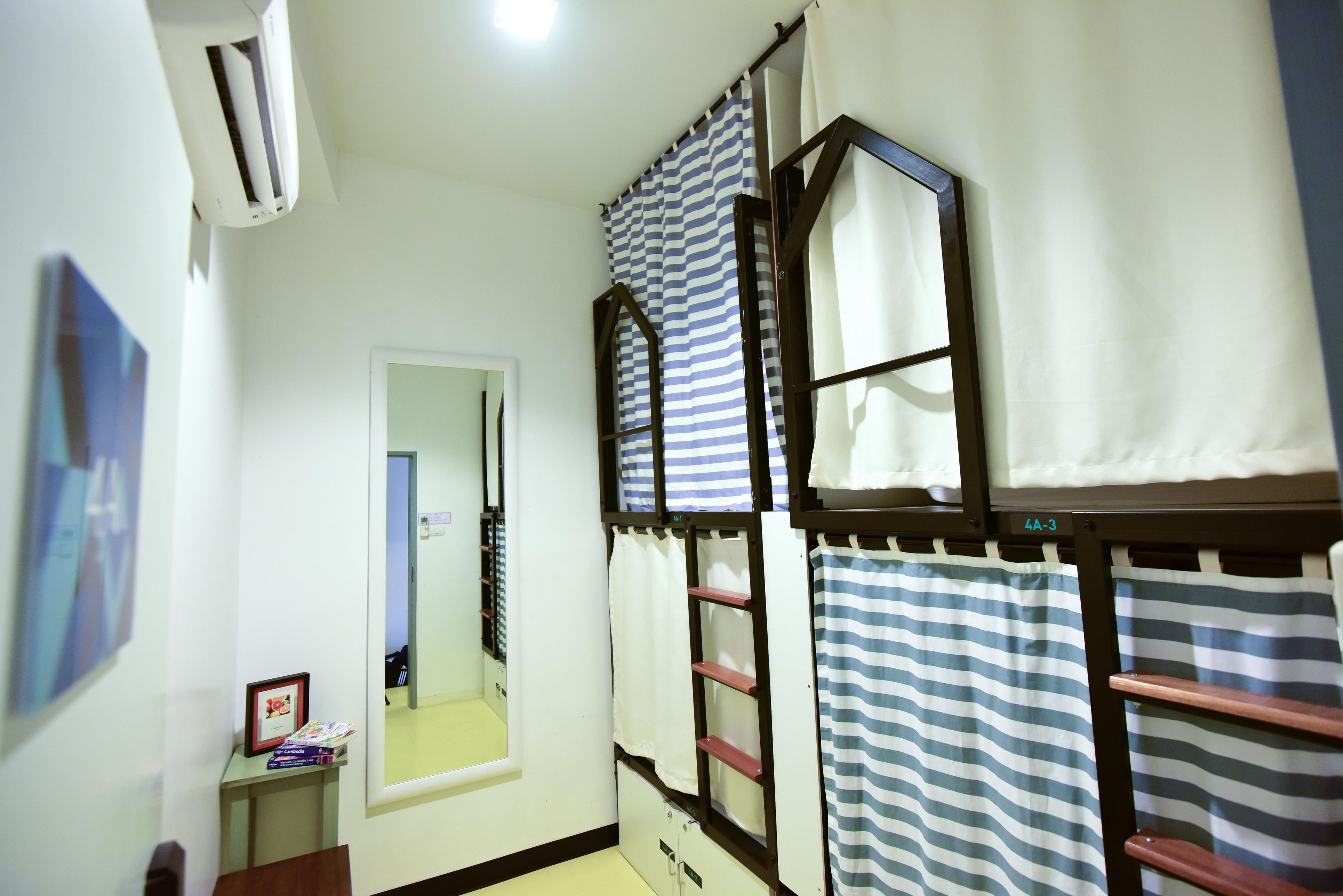 A dormitory room with bunk beds, a mirror, a small table with books, and an air conditioning unit.