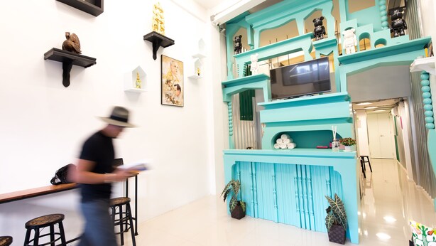A modern interior with a teal accent wall, a flat-screen TV, and a bar area with stools. - Vimarn Hostel (Bangkok)