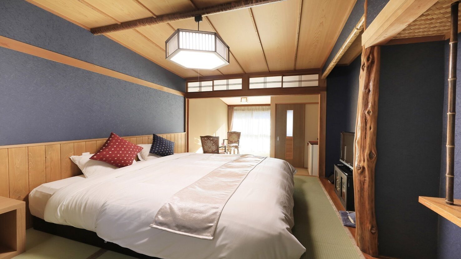 A hotel room with a large bed, wooden headboard, a television, and a traditional Japanese-style sliding door.