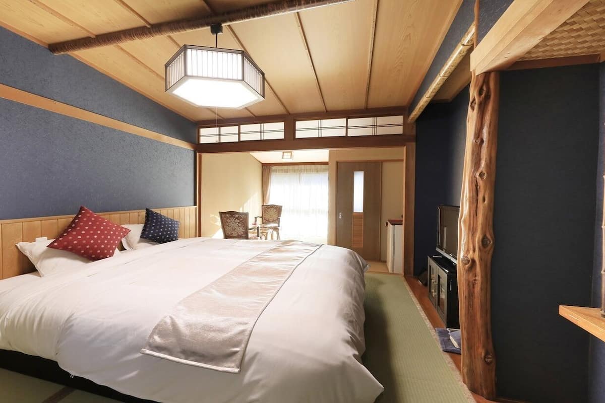 A hotel room with a large bed, wooden headboard, a television, and a traditional Japanese-style sliding door.