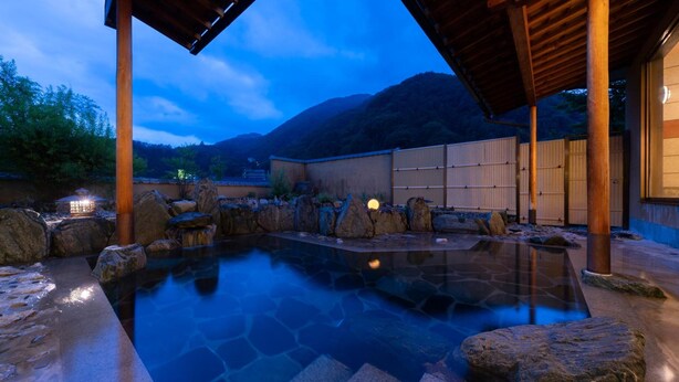 Ett traditionellt japanskt onsen med en pool av sten, träpelare och utsikt över berg i bakgrunden.