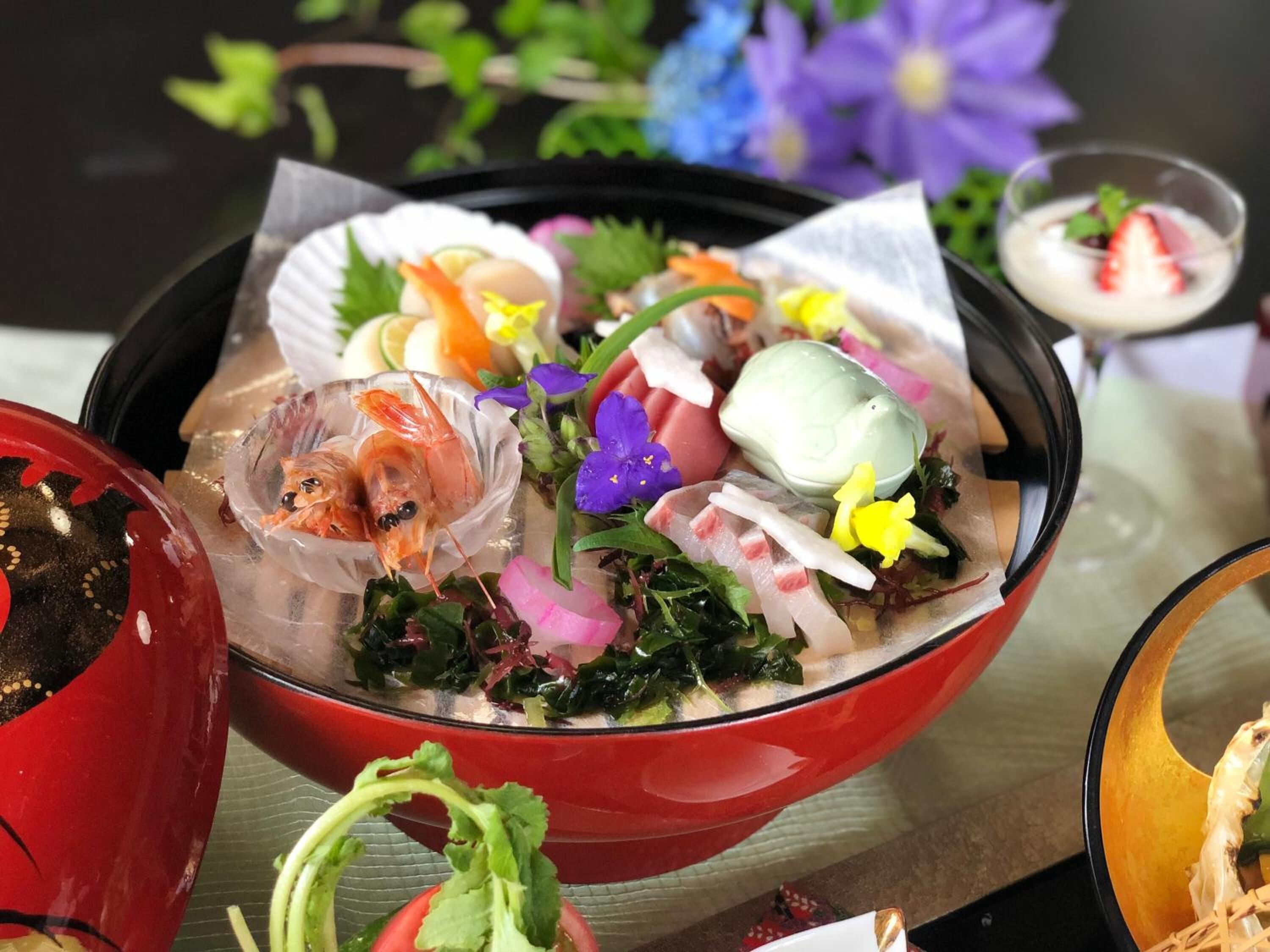 A bowl of food with various ingredients including seafood, vegetables, and a small cup of a creamy beverage.