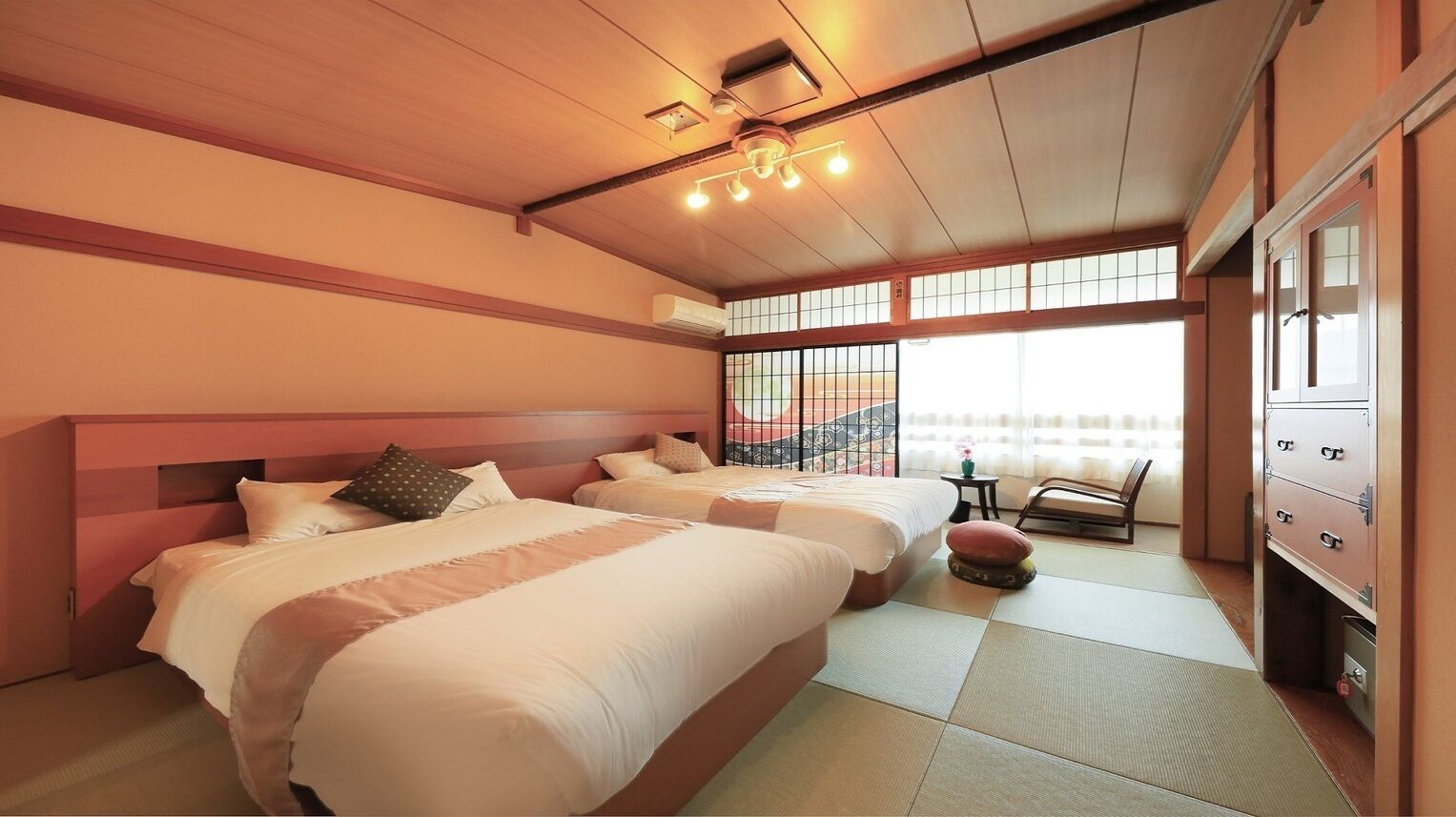 A hotel room with two beds, a small table, a chair, and a cabinet.