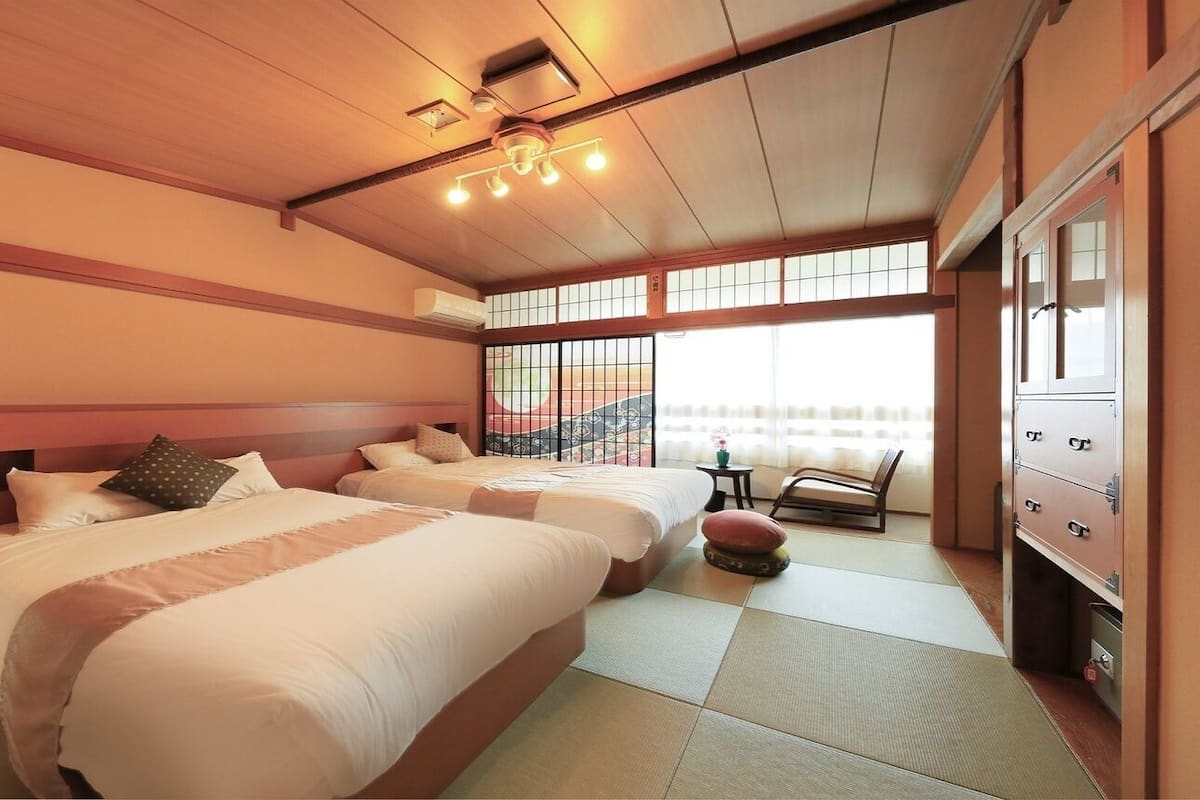 A hotel room with two beds, a small table, a chair, and a cabinet.