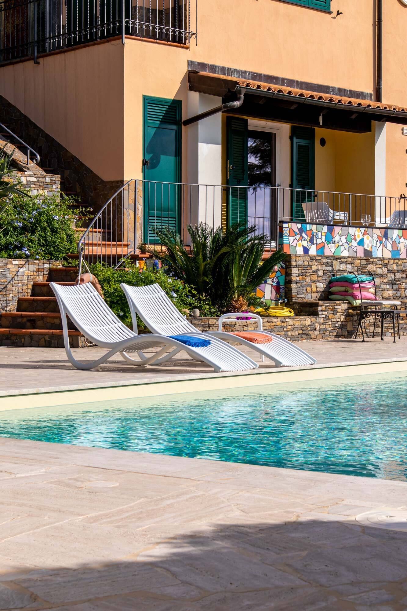 A swimming pool with lounge chairs, a stone staircase, and a tiled wall with colorful patterns.