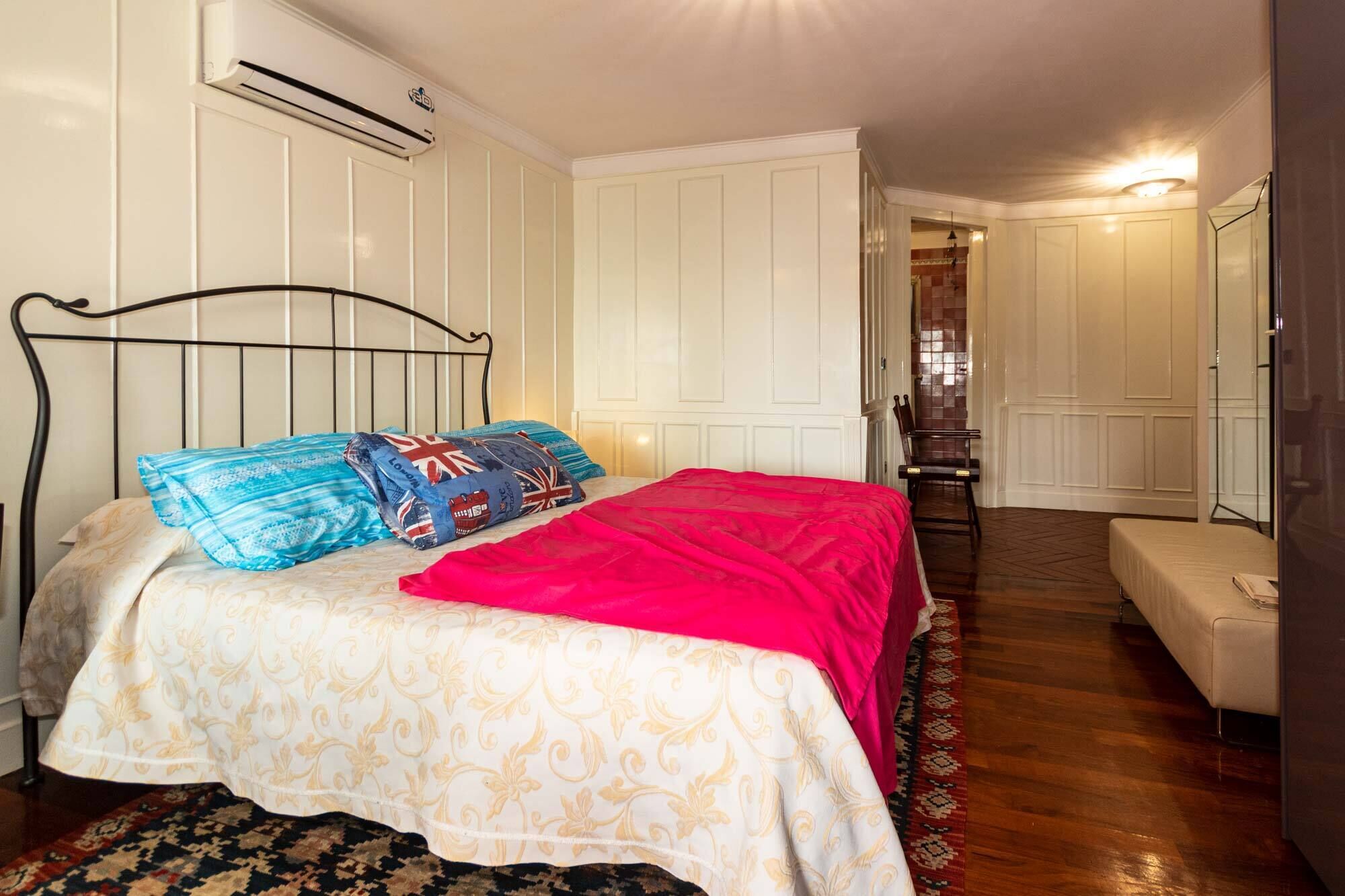 Une chambre à coucher comprenant un lit, une chaise, un banc et une porte donnant sur une autre pièce.